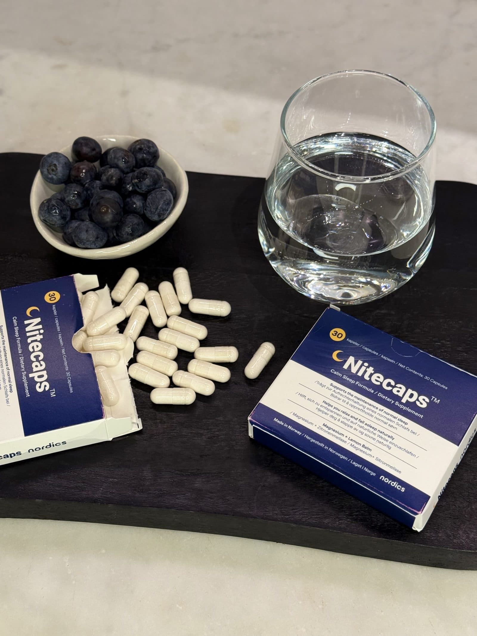Complemento alimenticio NiteCaps sin melatonina, con cápsulas y un vaso de agua.